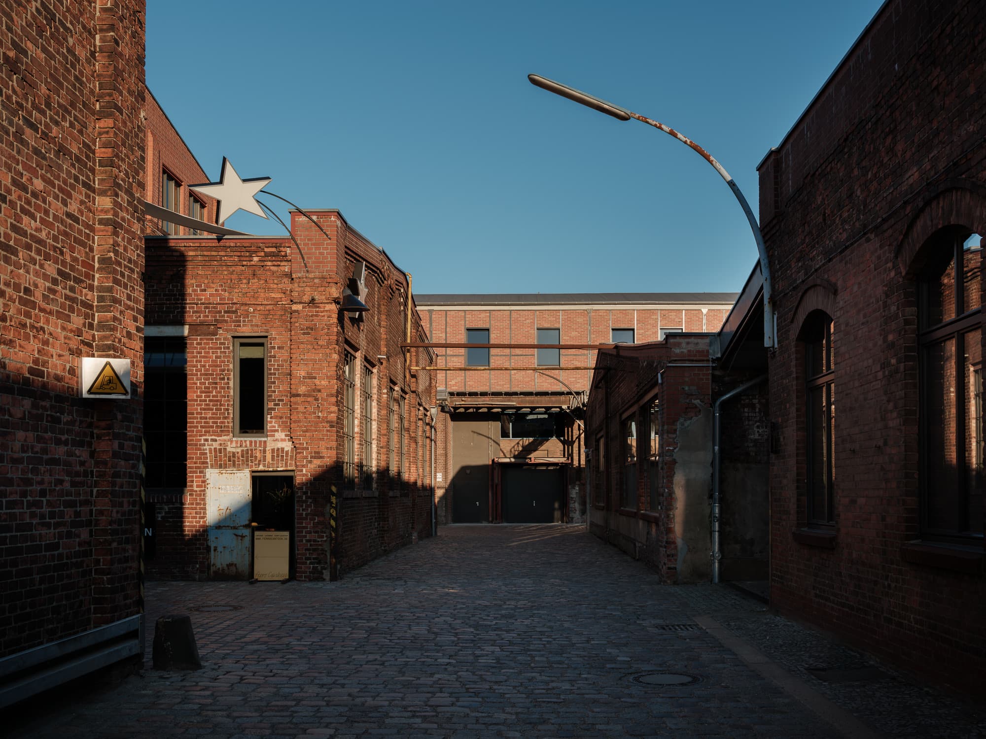The cobbled courtyard of Wilhelm Hallen between red brick factory buildings under a blue sky